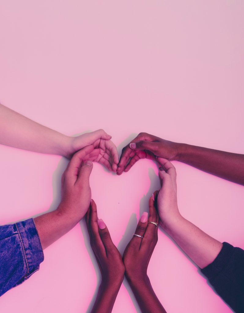 Image depicts six hands, of different skin colours and genders, all cupped and forming a silhouette of a heart.