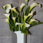 A vase of white lilies standing against a grey stone column.